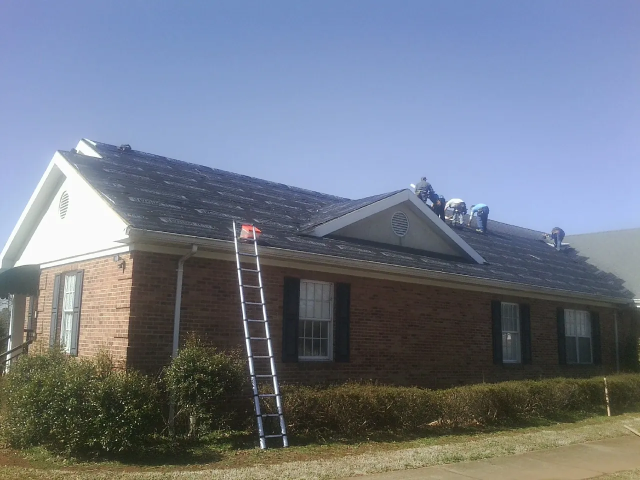 Crew tearing shingles off a brick ranch roof with a ladder set — Metal Roof Repair work by our crew in Tiverton