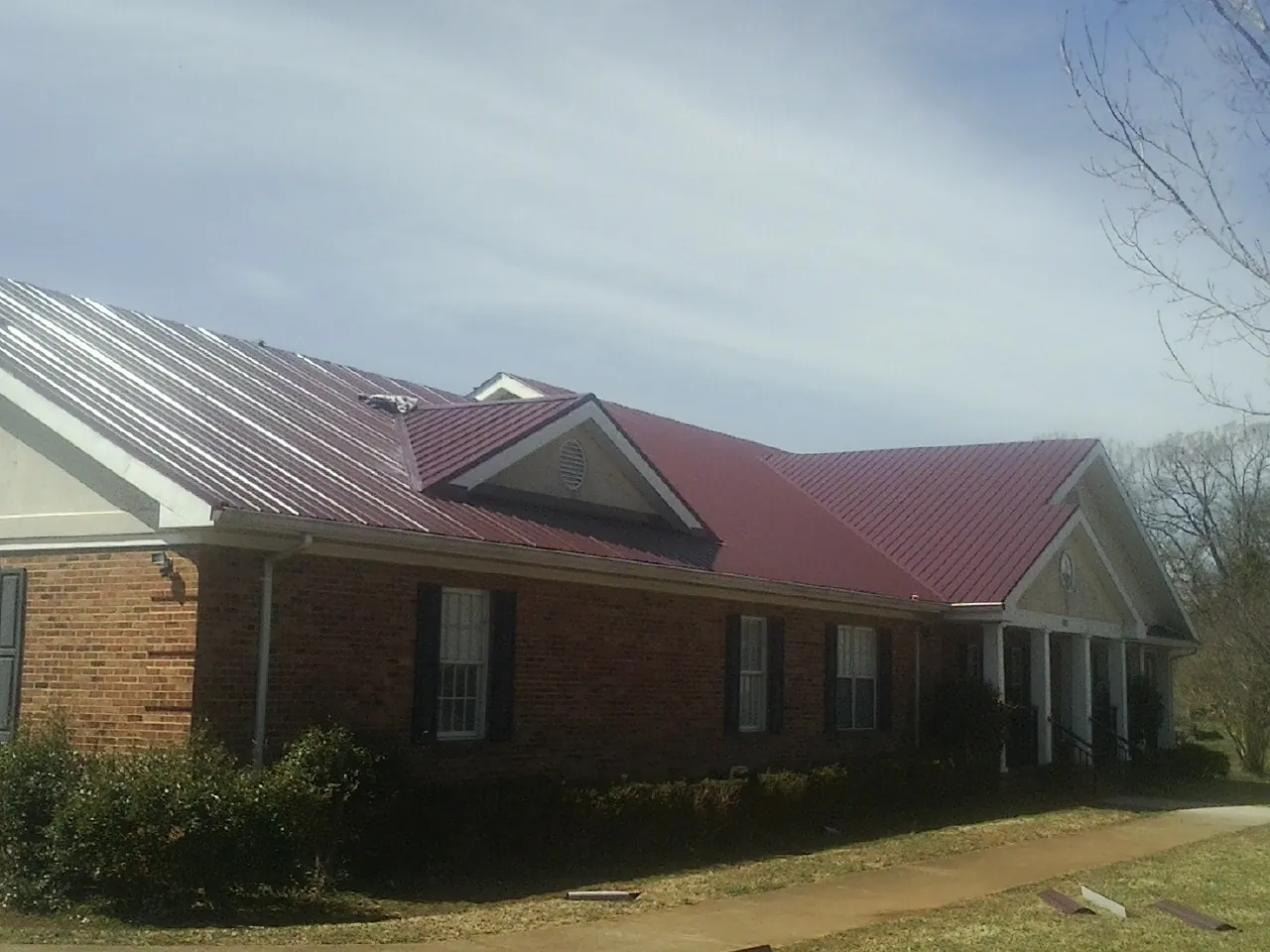 Red metal roof with gabled entries on a long brick building, from a Hail Damage Roof Repair job in Tiverton