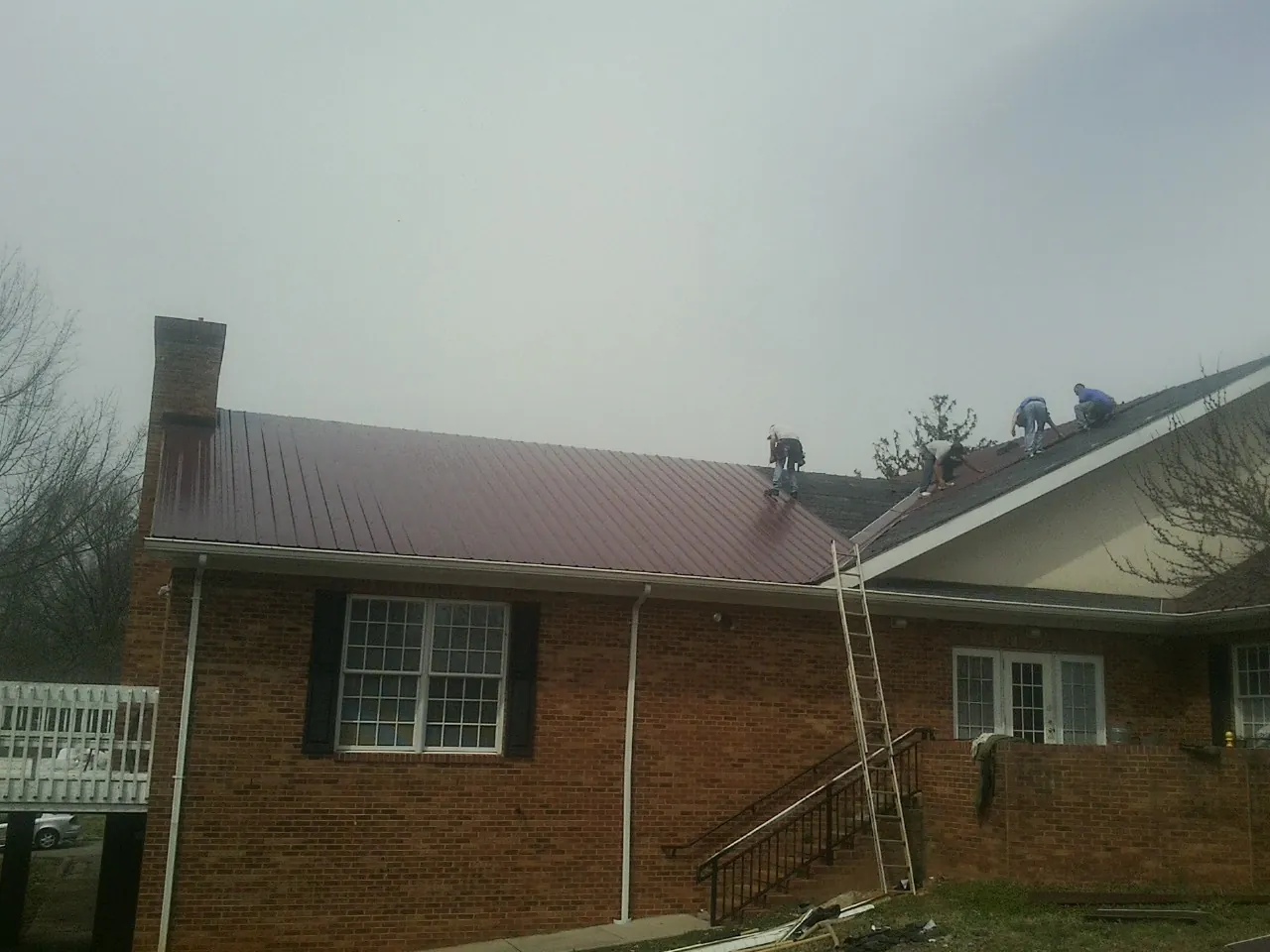 Crew setting red metal roofing panels on a brick home in Tiverton