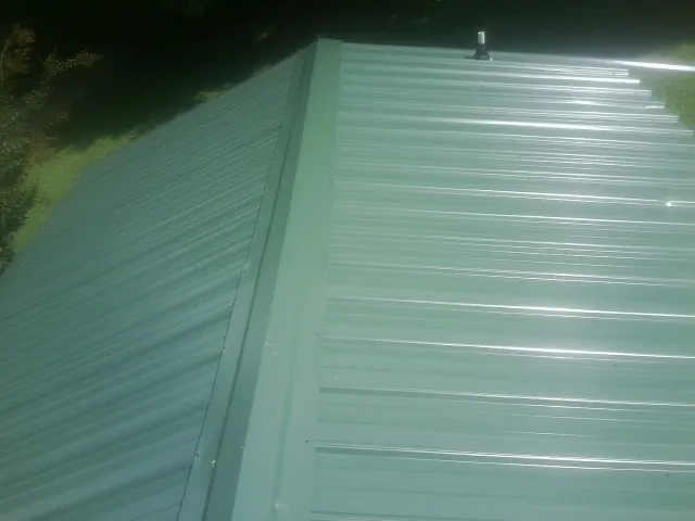 New green metal panels meeting at the ridge of a roof — Flat Roof Repair work by our crew in Tiverton