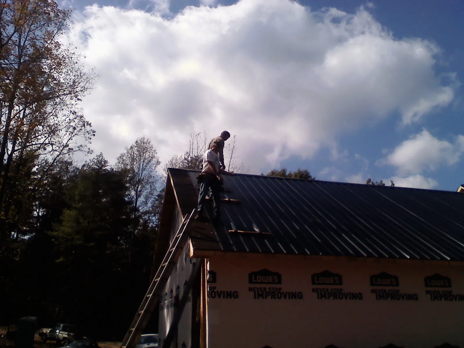 Roofer fastening dark metal panels high against a cloudy sky, from a Roof Inspection job in Tiverton