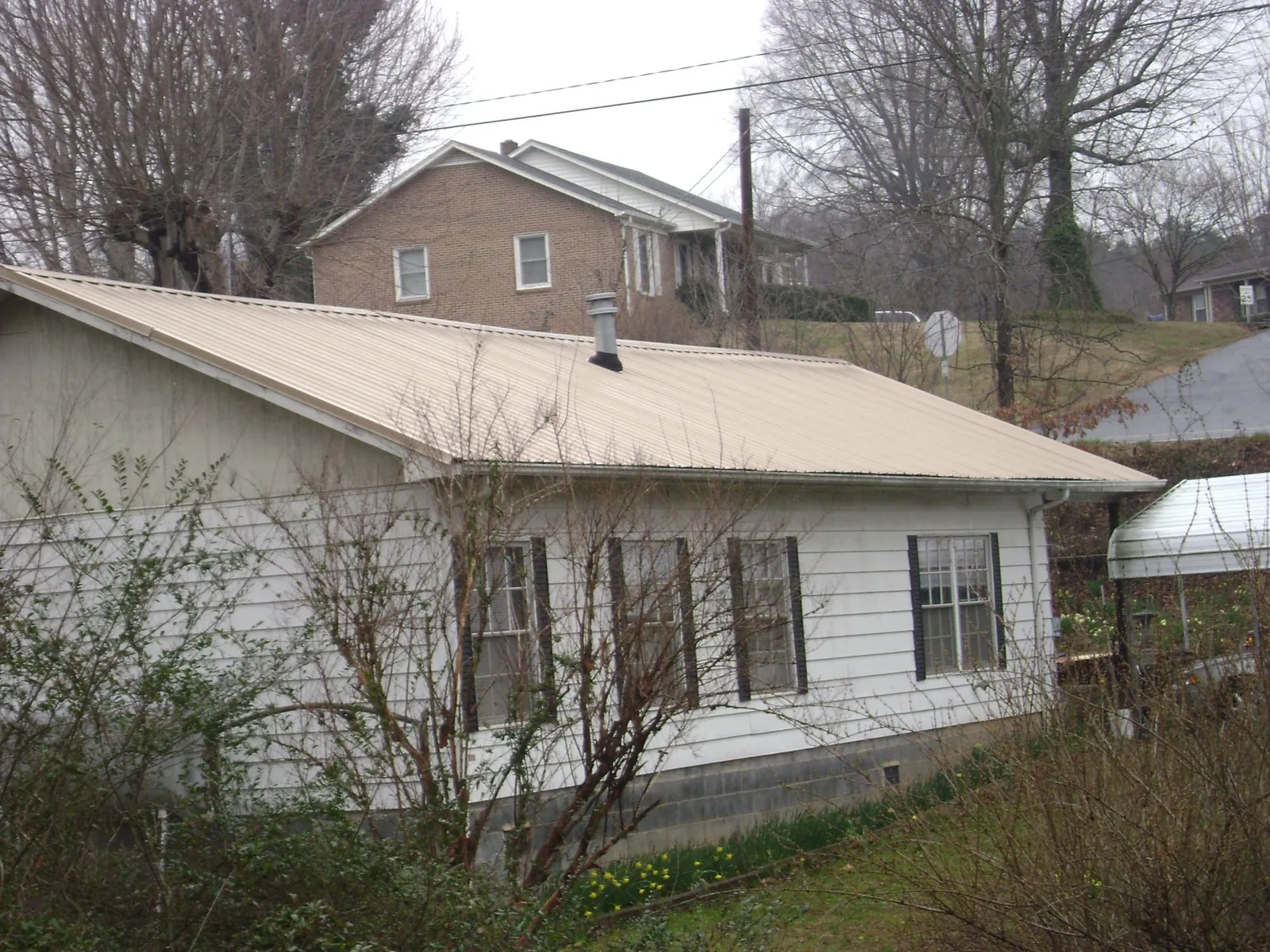 Tan metal roof on a white sided house set into a hillside — Commercial Roofing by Roofing Brothers in Tiverton
