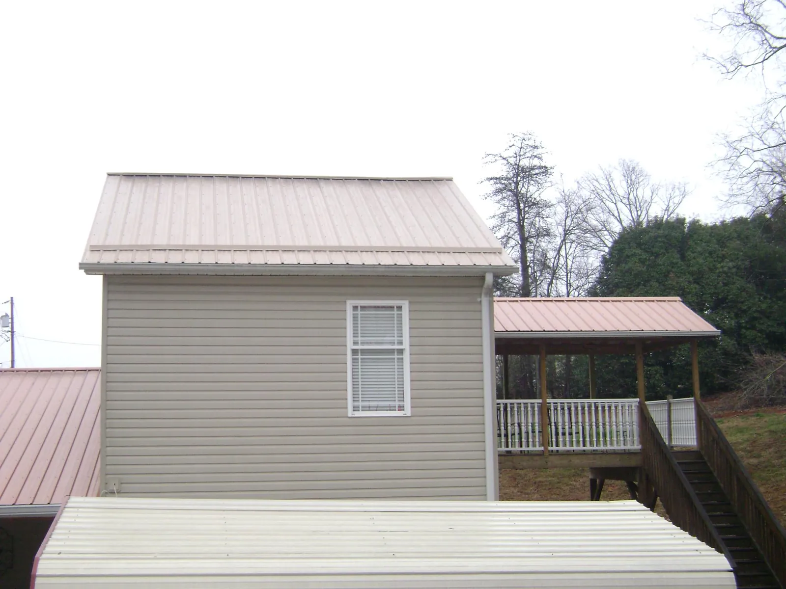 Tan metal roofs on a two story addition and attached porch, from a Roof Replacement job in Tiverton